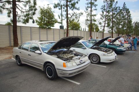 1995 Ford Taurus - Several cars are parked in a lot with their hoods open, displaying their engines.
