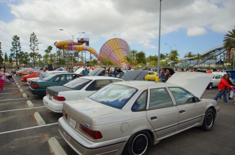 1995 Ford Taurus - A silver sedan is parked with its hood open at an outdoor car show, with a water slide in the background.