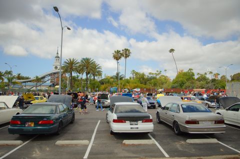 1995 Ford Taurus - Outdoor car show with many vehicles and attendees under a cloudy sky.