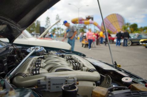 1995 Ford Taurus - Close-up of a V6 engine in an engine bay, with other vehicles and people in the background.