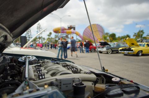 1995 Ford Taurus - Foreground engine bay at a car show with other vehicles and people in the background.
