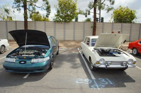 1995 Ford Taurus - Two cars with hoods open are parked in a lot. One is a green 1995 Ford Taurus.