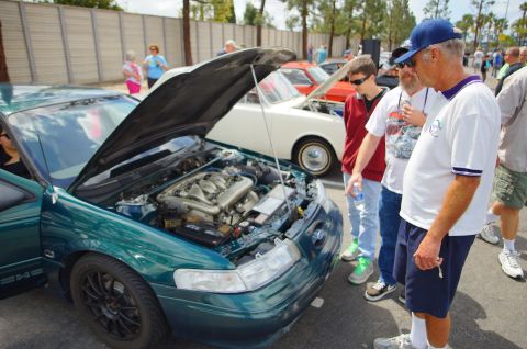 1995 Ford Taurus - A group of men examine the engine of a green 1995 Ford Taurus at a car show.