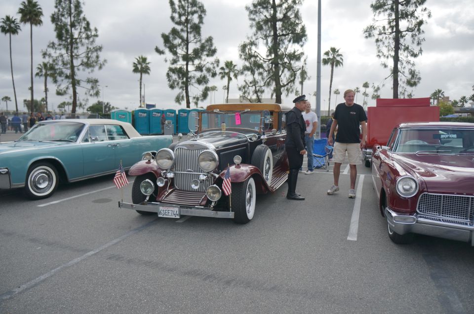 dark colored vintage convertible with a man in uniform standing next to it. Two other cars are parked nearby