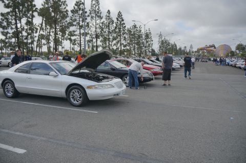 1995 Ford Taurus - A white coupe has its hood open while parked at an outdoor car show event.