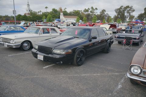 1995 Ford Taurus - Black sedan with custom hood scoop and wheels at a car show, parked next to other vehicles.