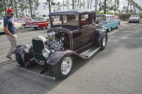 1995 Ford Taurus - A custom hot rod coupe is displayed at a car show with other classic vehicles in the background.