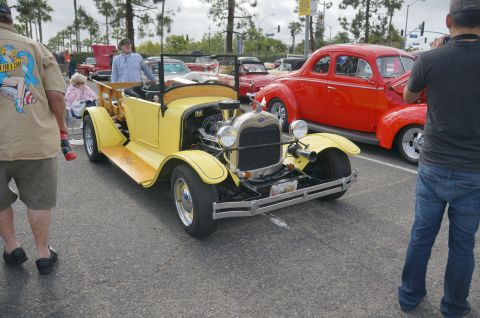 1995 Ford Taurus - A yellow hot rod truck is parked at an outdoor car show with other vehicles and spectators.