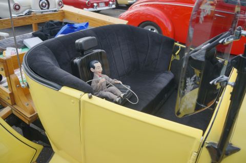 1995 Ford Taurus - A doll sits in the passenger seat of a vintage yellow car, with other classic vehicles in the background.
