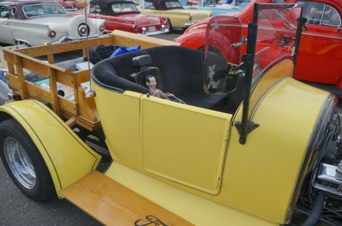 1995 Ford Taurus - A yellow hot rod with a wooden bed is parked among other classic cars, with a doll seated in the driver's position.