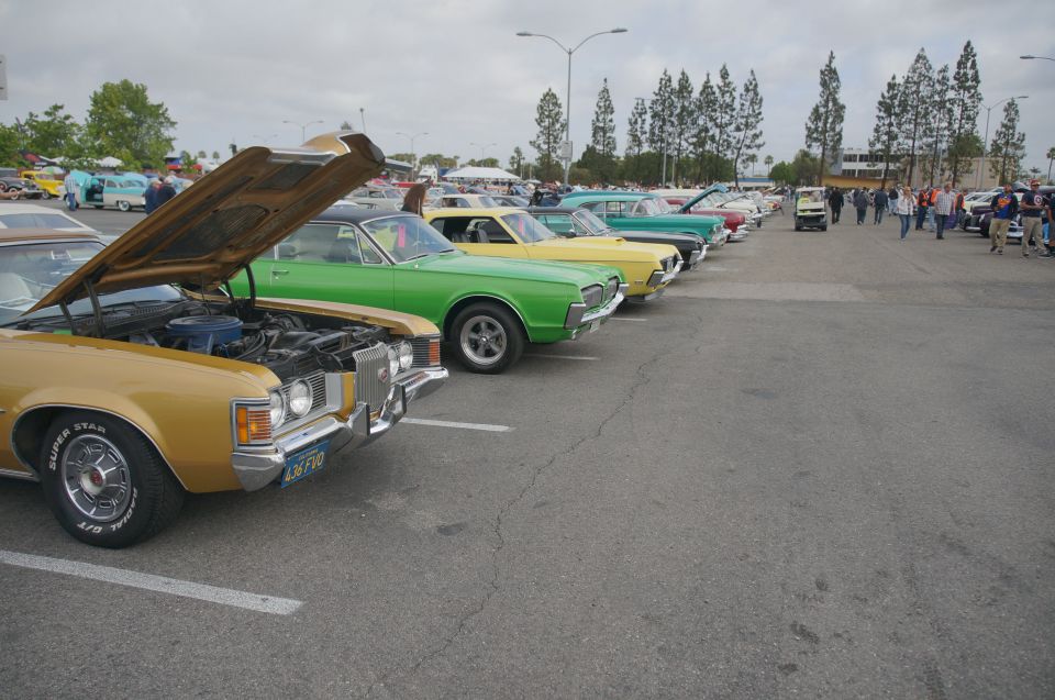 Gold classic car with hood open, parked in a line with other vintage cars. License plate reads L8FVO