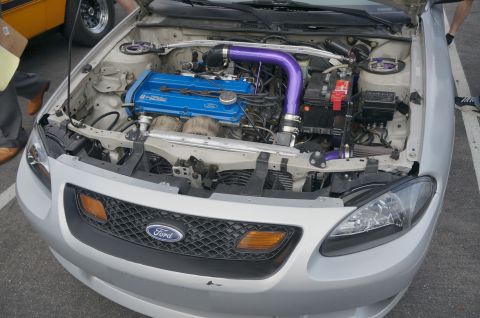 1995 Ford Taurus - The engine bay of a silver car shows a blue Ford engine with custom purple intake piping and a strut bar.