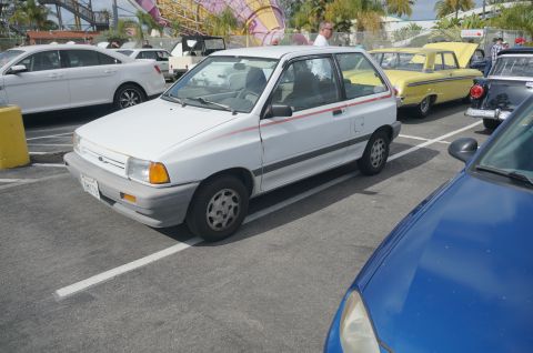 1995 Ford Taurus - A white hatchback is parked in a lot with other vehicles, including a yellow sedan and a blue car in the foreground.