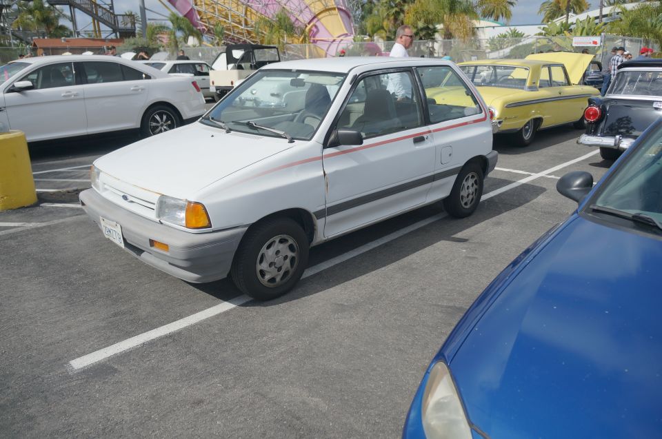 White hatchback car with red stripe, parked in a lot. Front bumper is gray, wheels are silver with five spokes