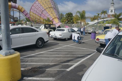 1995 Ford Taurus - A white sedan is parked at an outdoor event, with a large water slide structure visible behind it.