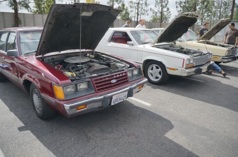 1995 Ford Taurus - A maroon sedan from the 1980s with its hood open sits in a parking lot next to other vehicles.
