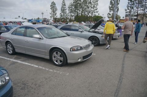 1995 Ford Taurus - A silver sedan is parked in a lot with other vehicles and people around.