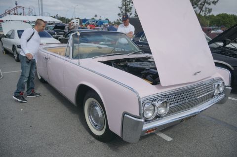 1995 Ford Taurus - A classic pink convertible with its hood open is displayed at a car show, with other vehicles visible in the background.