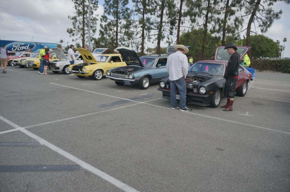 Several cars parked in a lot, some with hoods open, people standing around them