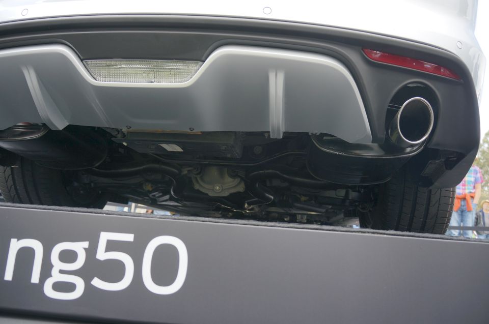 Rear bumper and exhaust pipe of a car, with visible undercarriage and tires. Text 'ng50' is on a platform below
