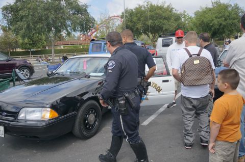 1995 Ford Taurus - A police car is parked in a lot with several people gathered around it.