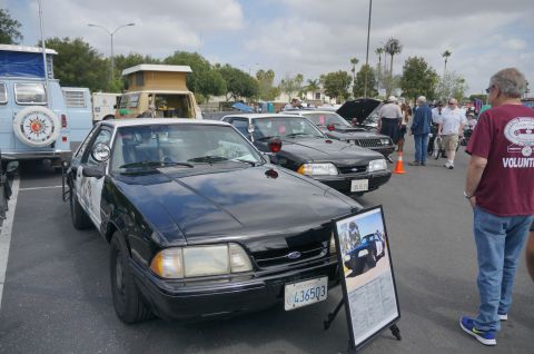 1995 Ford Taurus - A black and white police car is parked at a car show, with other vehicles and people in the background.