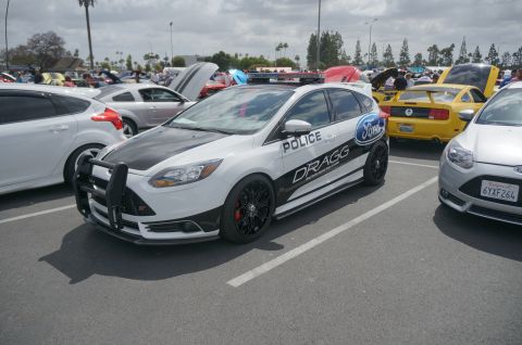 1995 Ford Taurus - A modified Ford Focus, styled as a police car, is displayed at an outdoor event with other vehicles.
