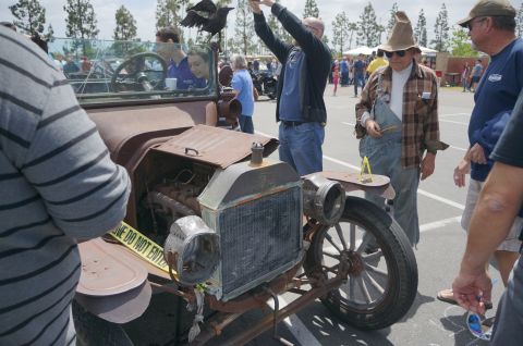 1995 Ford Taurus - A group of people gather around a very old, rusty car at an outdoor event.