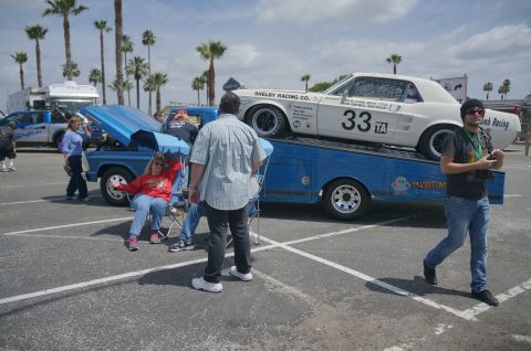 1995 Ford Taurus - A white 1967 Ford Mustang race car is loaded onto a blue car carrier, with other vehicles and people in the background.