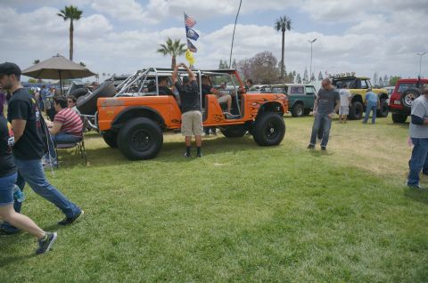 1995 Ford Taurus - Outdoor car show features a customized orange off-road vehicle with flame decals and a roll cage.