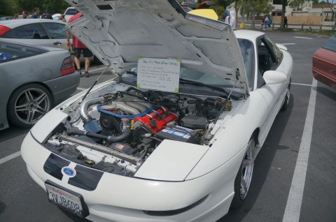 1995 Ford Taurus - A white sports coupe is parked with its hood open, revealing the engine bay and a sign with vehicle details.