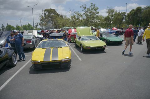 1995 Ford Taurus - A yellow De Tomaso Pantera is parked at a car show, with other vehicles and people around.