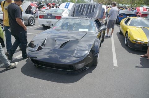 1995 Ford Taurus - A black sports car is displayed with its hood open at a car show, alongside other vehicles.