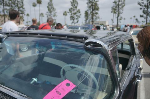 1995 Ford Taurus - A black car with chrome trim and a white steering wheel is parked outdoors with other vehicles and people.