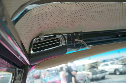 1995 Ford Taurus - Close-up of a car's interior air vent and grab handle, with a blurred background showing multiple vehicles at an outdoor event.