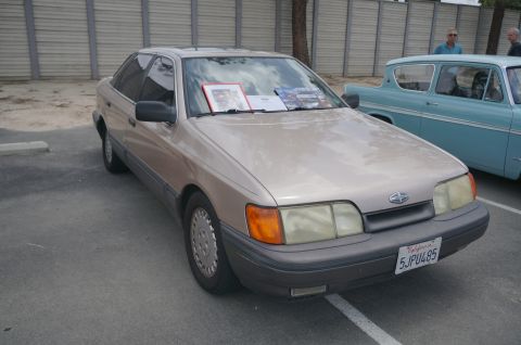 1995 Ford Taurus - Tan 1985 Ford Granada sedan at a car show, with a blue classic car visible to the right.
