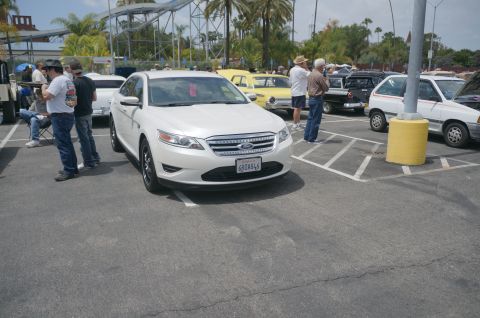1995 Ford Taurus - A white Ford sedan is parked in a lot with other vehicles and people around.