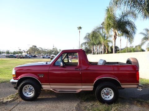 1994 Ford Bronco - Side view of a red 1994 Ford Bronco with tan trim and a spare tire in the cargo area.