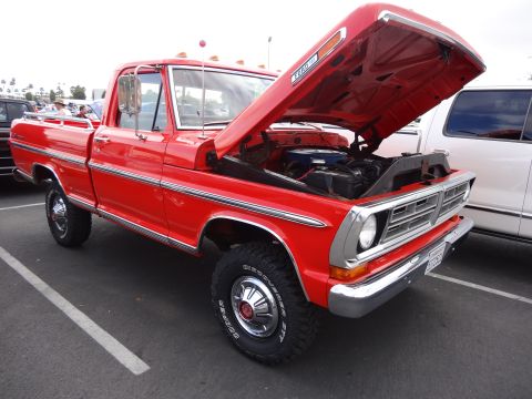 1994 Ford Bronco - This red Ford pickup truck displays a prominent chrome grille and side trim, with its hood open to reveal the engine.