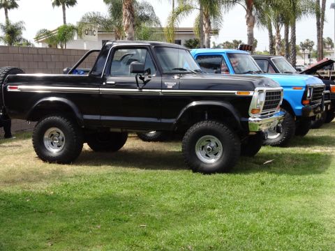 1994 Ford Bronco - A line of trucks, including a black Ford Bronco, are parked on a grassy area.
