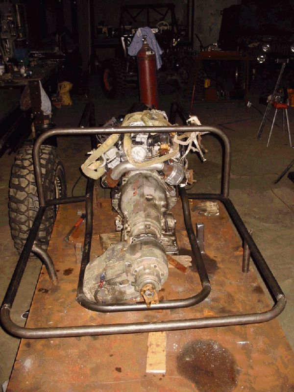 Engine, transmission, and transfer case mocked up in a bare tube chassis in a workshop