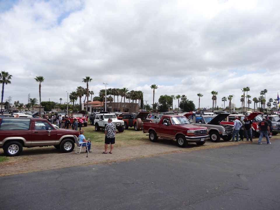 Maroon 1994 Ford Bronco parked next to other vehicles and people at an outdoor event