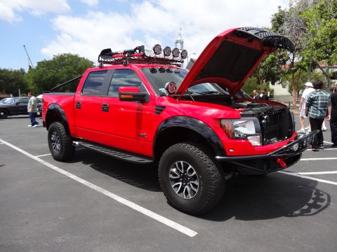 1994 Ford Bronco - A red pickup truck is parked with its hood open, equipped with a roof rack and auxiliary lights.