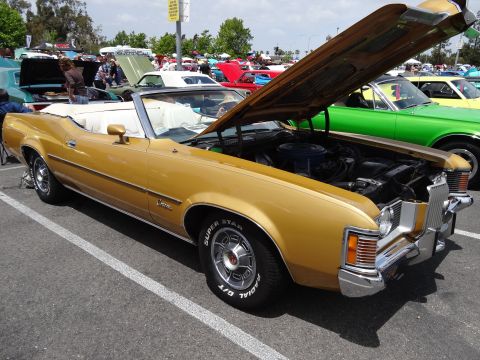 1994 Ford Bronco - A gold convertible is displayed with its hood open, revealing the engine compartment. Other vehicles are visible in the background.