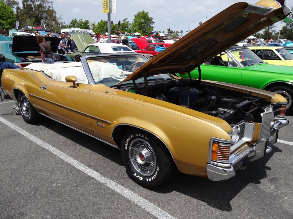 Gold convertible with hood open, showing engine. Visible text on tire