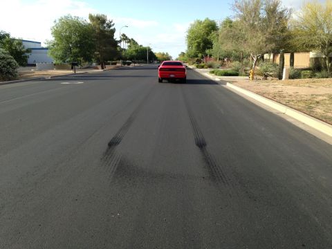 2010 Dodge Challenger - A red Dodge Challenger is seen from behind on a suburban street, with prominent tire marks on the asphalt.