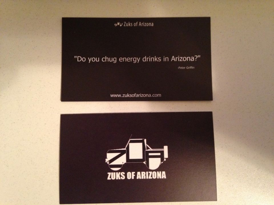 Two black business cards. Top card has text and a website. Bottom card has a stylized drawing of a vehicle and text