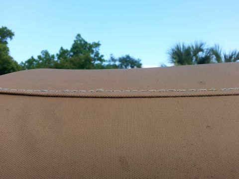 1992 Ford Bronco - Close-up of a tan canvas soft-top or cover showing a stitched seam, with trees and palm against a blue sky behind.
