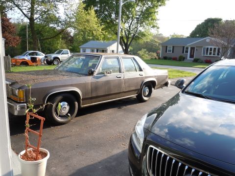 2001 Ford Crown Victoria - An older brown sedan is parked in a driveway with other vehicles visible in the background.