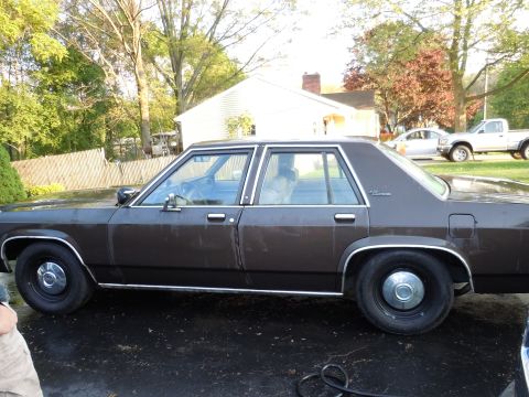 2001 Ford Crown Victoria - Side view of a brown Ford sedan, likely from the 1980s, with other vehicles in the background.